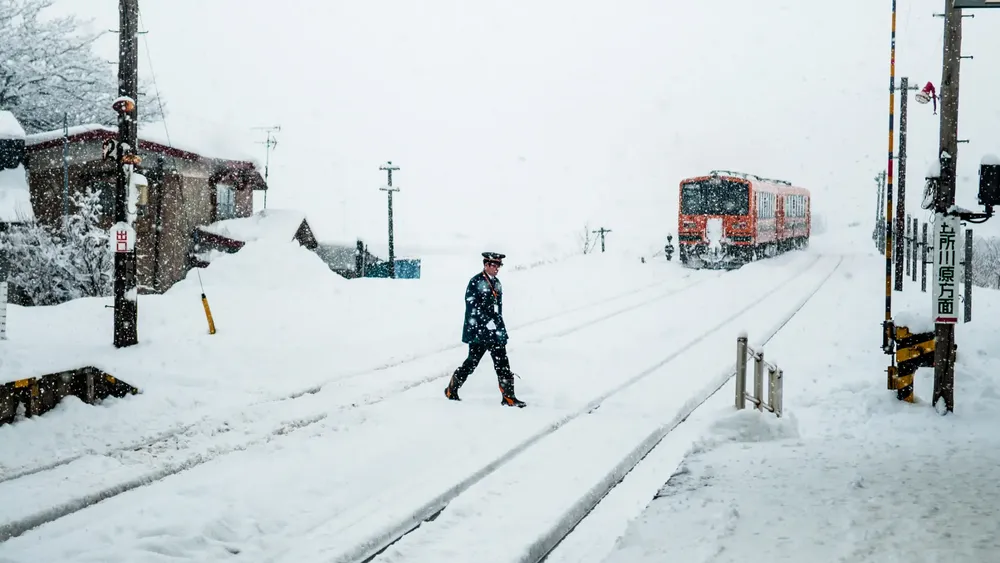 oficial-de-conductor-de-tren-a-pie-cruzan-las-vias-del-ferrocarril-tsugaru-en-la-nieve-del-invierno-en-la-estacion-de-goshogawara-en-aomori-japon